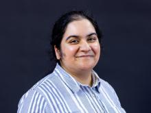 A person with dark hair in a collared shirt smiling.