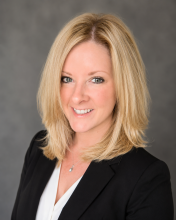 A person with blonde hair in a black suit jacket smiling.